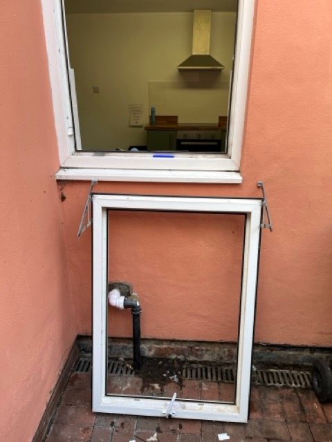 Broken white window frame leaning against an orange wall below an open window with a kitchen inside