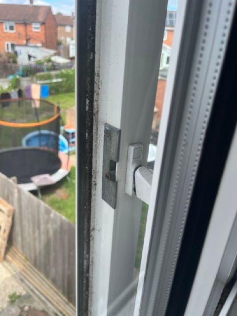 Open window latch with a backyard view, including a trampoline and fence.