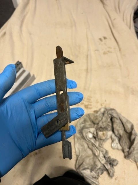 Gloved hand holding a small rusted metal tool against a white cloth background