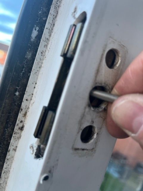 Hand inserting a metal latch bolt into a white door strike plate near a blue door frame