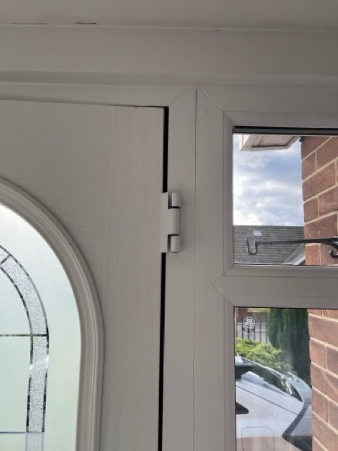 White front door with arched glass and side window showing a street outside.