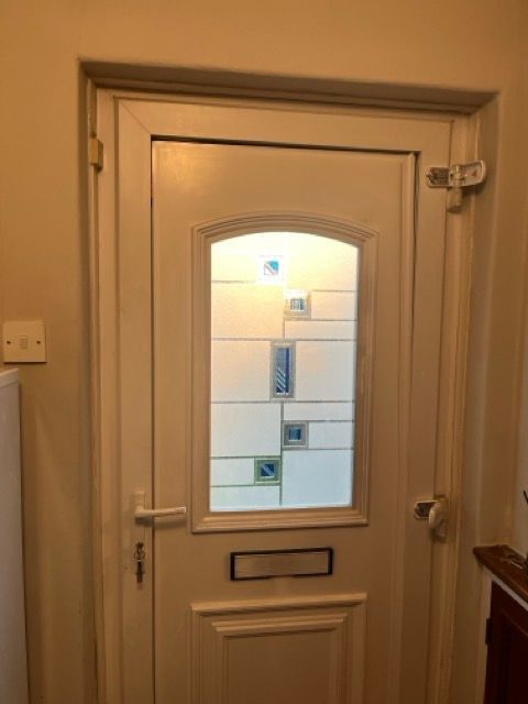 Cream front door with a small window, mail slot, and silver handle in an indoor hallway.