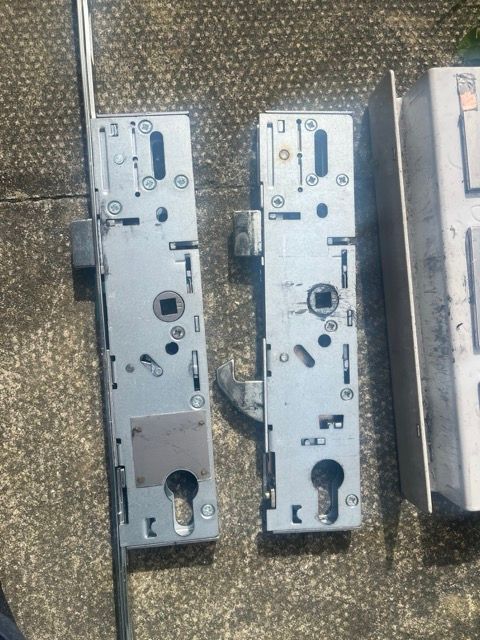Two silver metal door latch mechanisms laid side by side on a textured work surface.