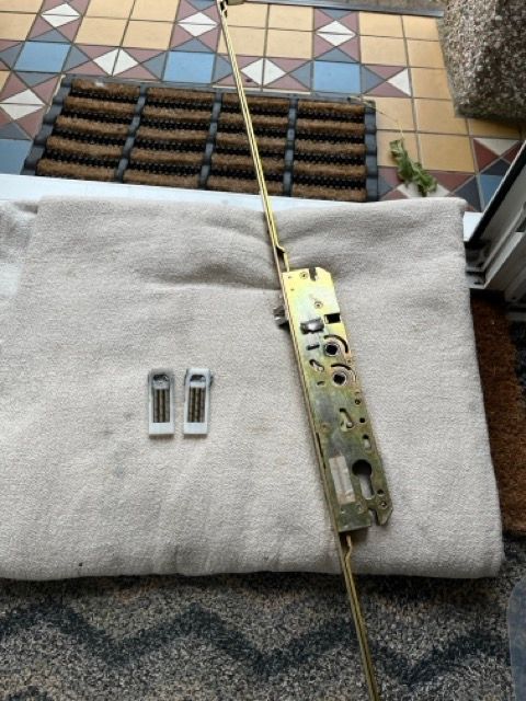 Door lock mechanism and two small metal parts on a white towel over a patterned rug.