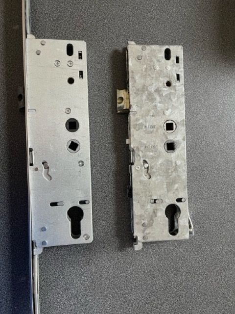 Two metal door lock plates side by side on a gray surface