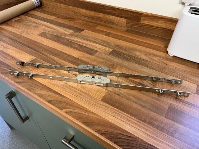 Two metal sash window stays on a wooden countertop in a kitchen.