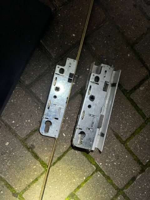 Two silver metal door lock plates lying on a brick pavement, lit by a flashlight.