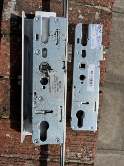 Two metal door lock mechanisms laid side by side on a brick surface.