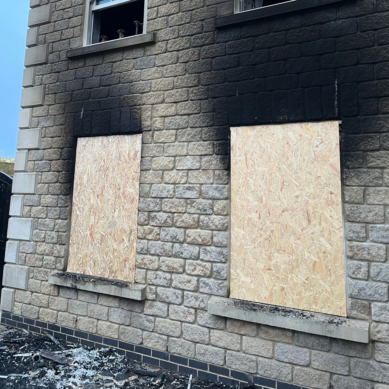 Exterior of a stone building with boarded-up windows and soot damage from a fire.