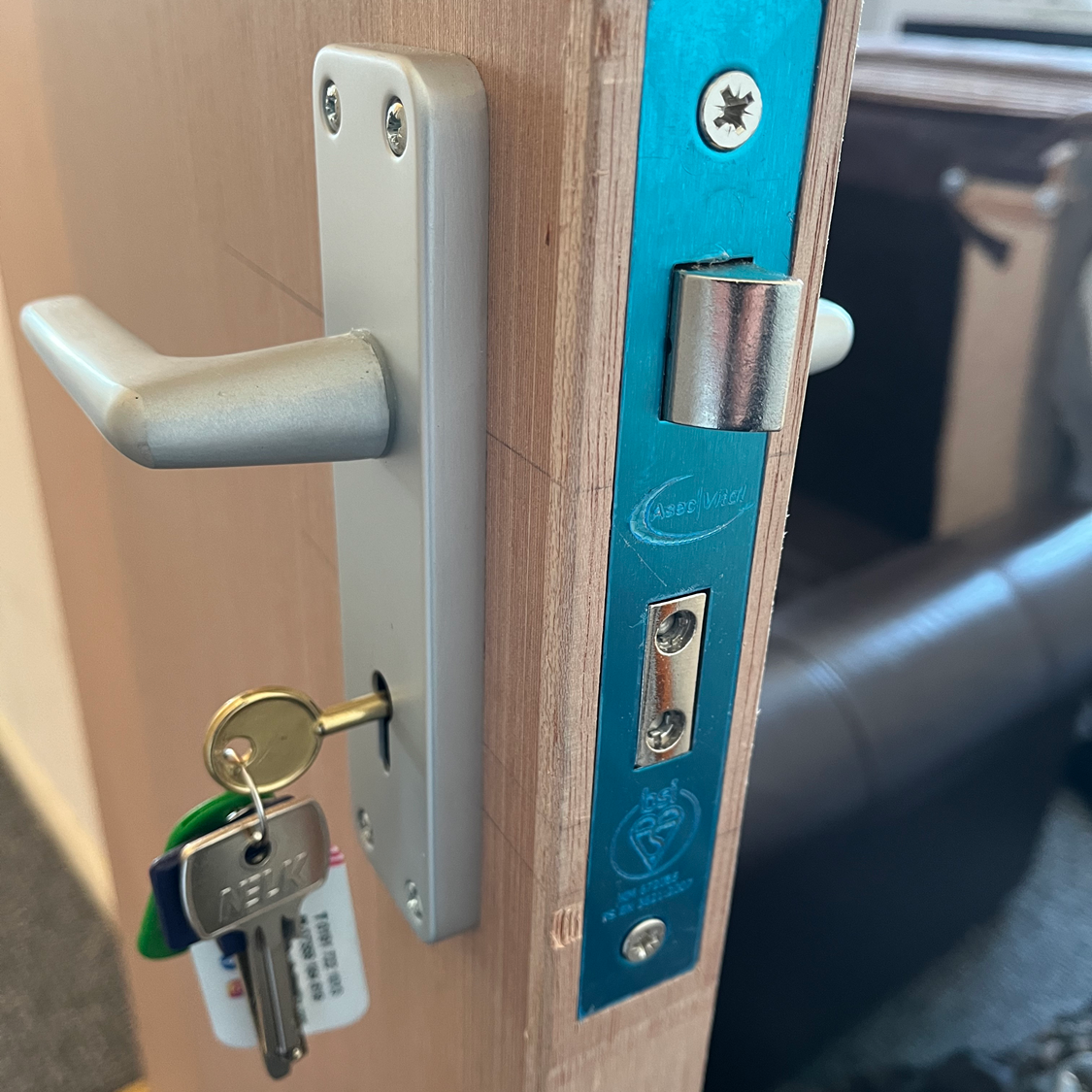Silver door handle with key inserted, on a light wood door with blue lock plate.