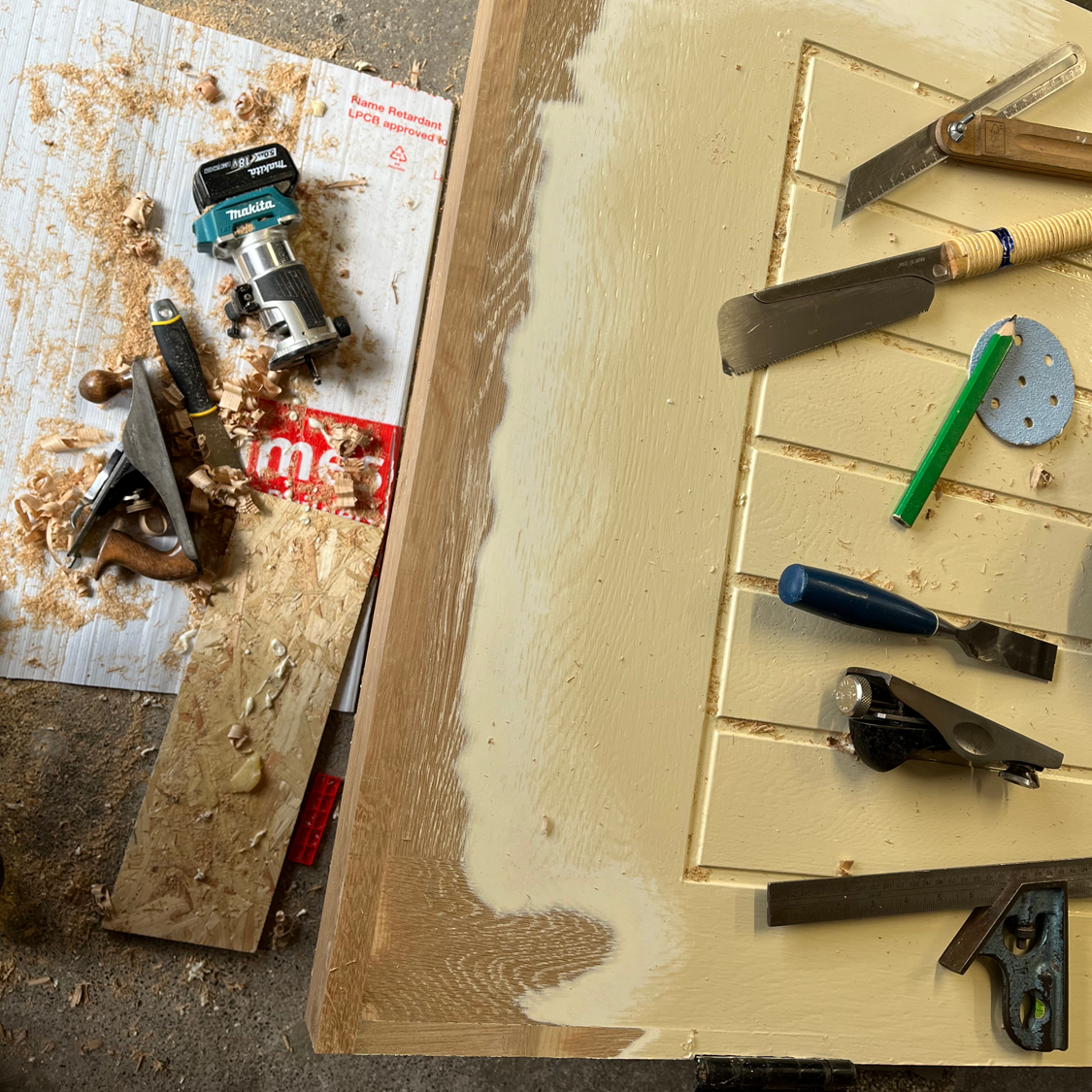 Woodworking tools on a partially painted wooden door, including a router, plane, chisels, and a pencil.
