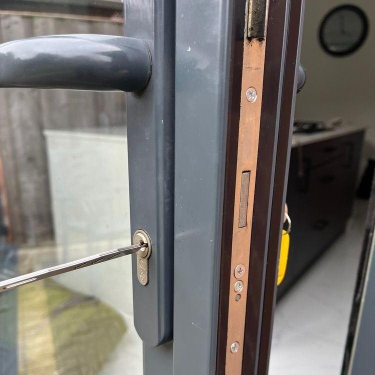 A person is using a screwdriver to unlock a door lock. The door frame is gray, and the lock is silver.