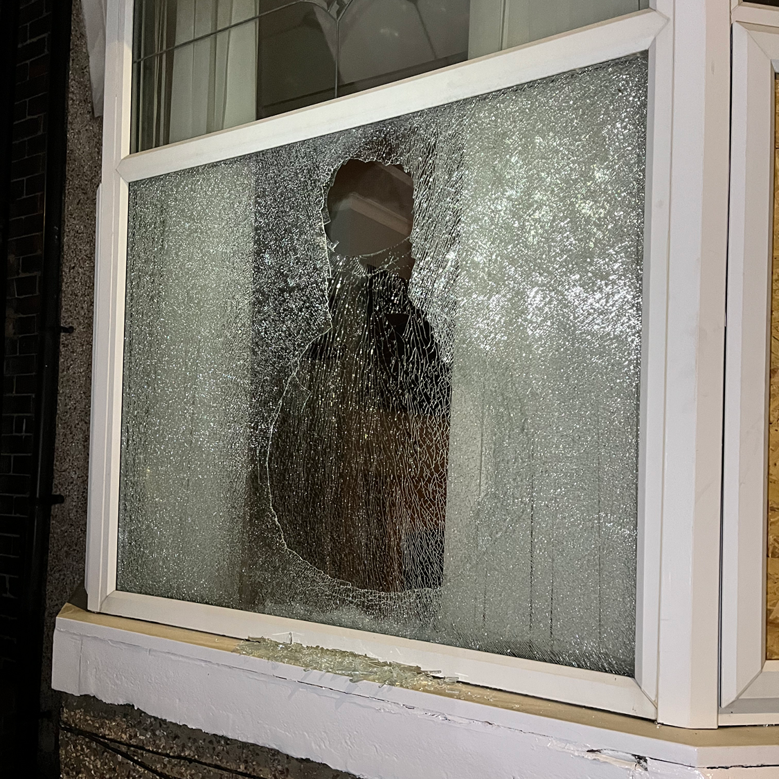 Broken window pane; hole in glass, white frame. Exterior view.