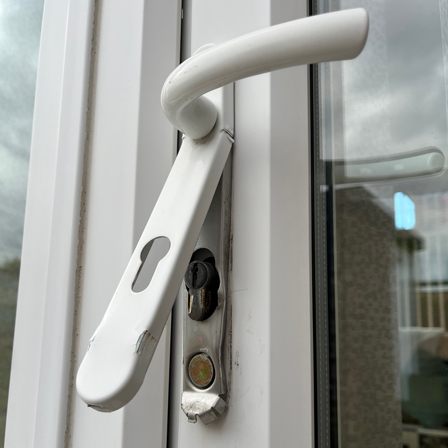 White window handle with keyhole, slightly damaged, on a white window frame.
