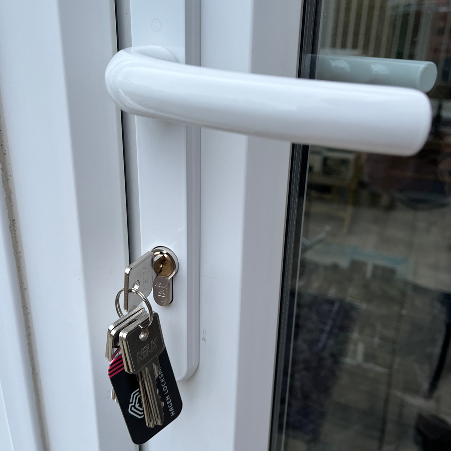 White door handle with keys in the lock. The handle is pulled up and the keys are hanging.