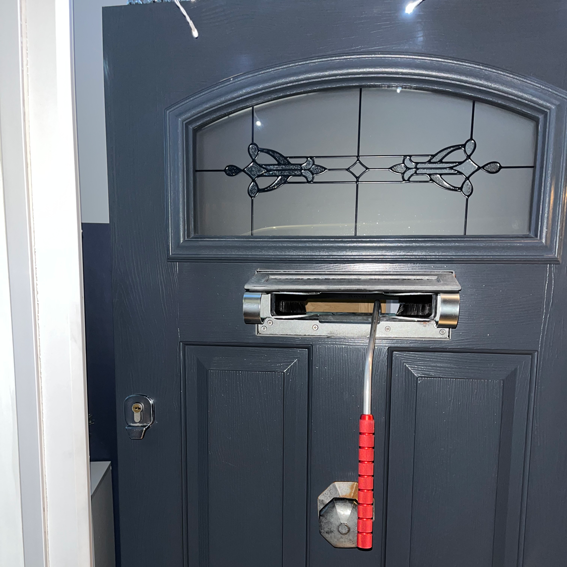 Dark gray front door with decorative glass, mailbox, and a red-handled tool stuck in the mail slot.