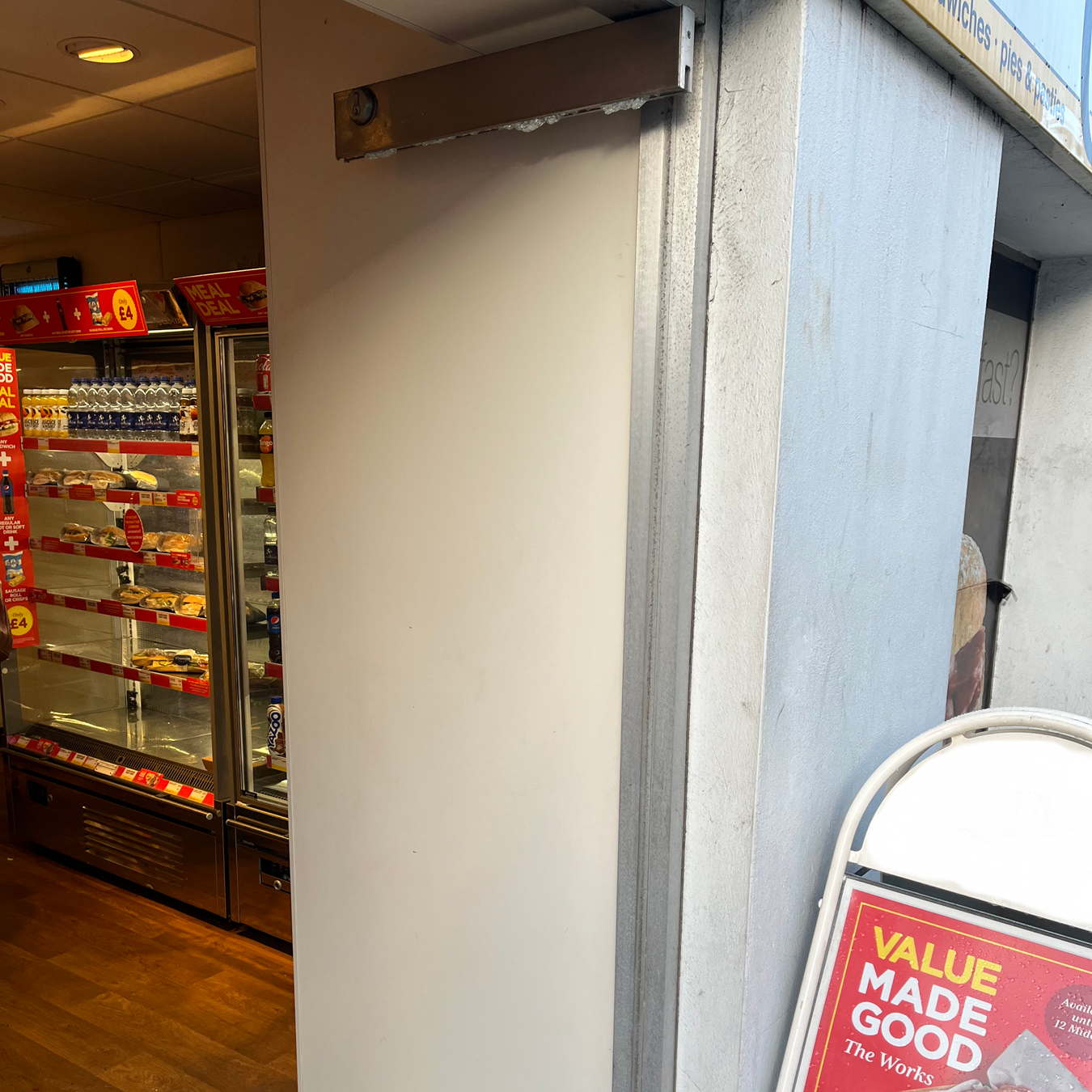 Inside a shop, a vending machine is visible. A white wall is next to an outside sign.