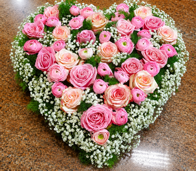 Composizione a forma di cuore di rose rosa e crema con gypsophila bianca su una superficie marrone.