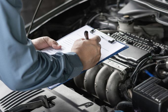 Un meccanico prende appunti su un blocco per appunti accanto al motore di un'auto in un'officina.