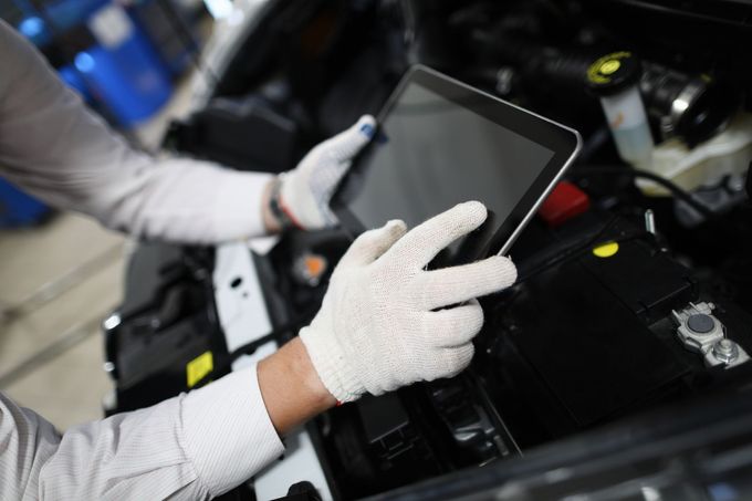Un operaio con i guanti utilizza un tablet per ispezionare macchinari in un ambiente industriale.