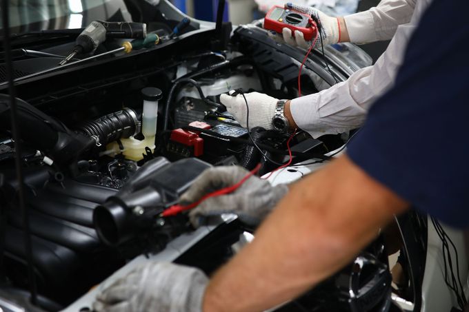 Meccanico al lavoro sotto il cofano aperto di un'auto con degli attrezzi in un'officina.