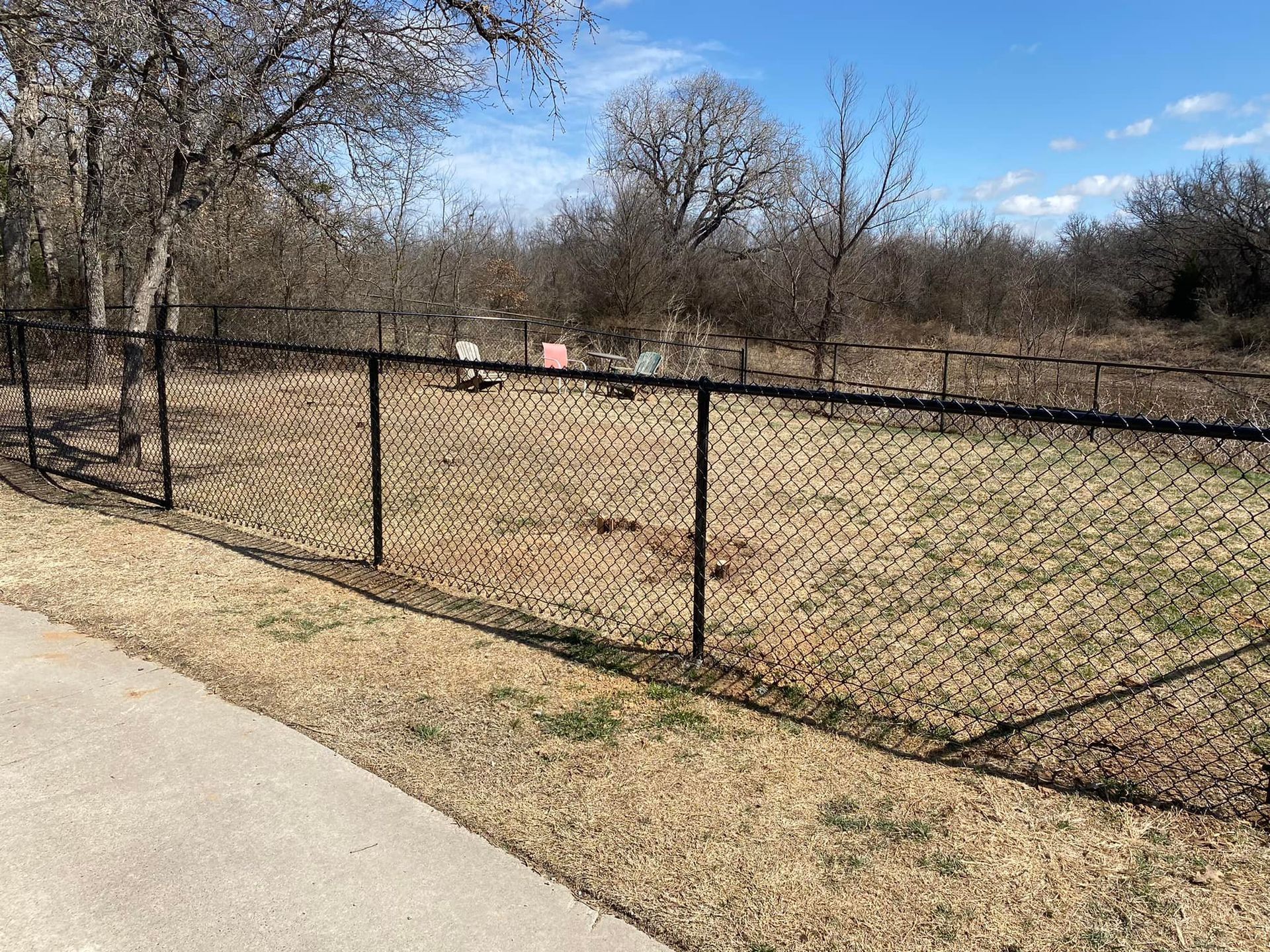 A chain link fence surrounds a field with trees in the background.