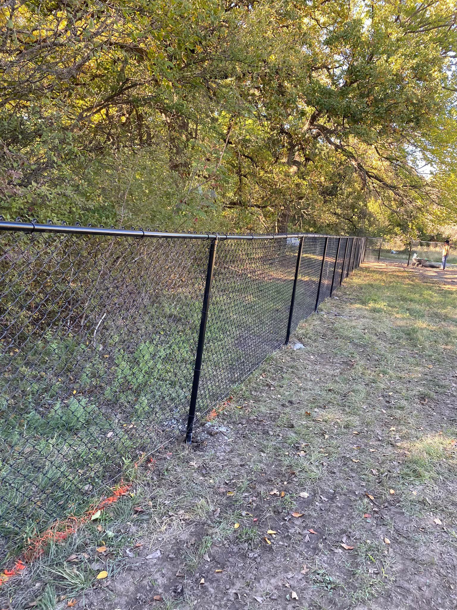 A black chain link fence is surrounded by trees and grass in a park.