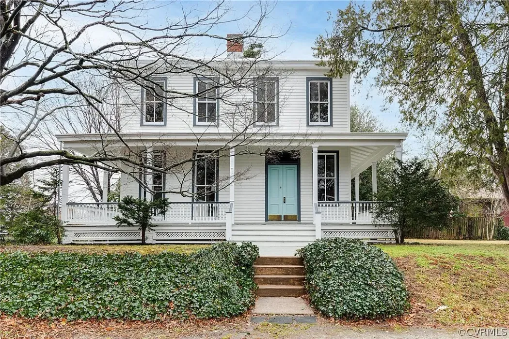 A large white house with a blue door and porch surrounded by trees.