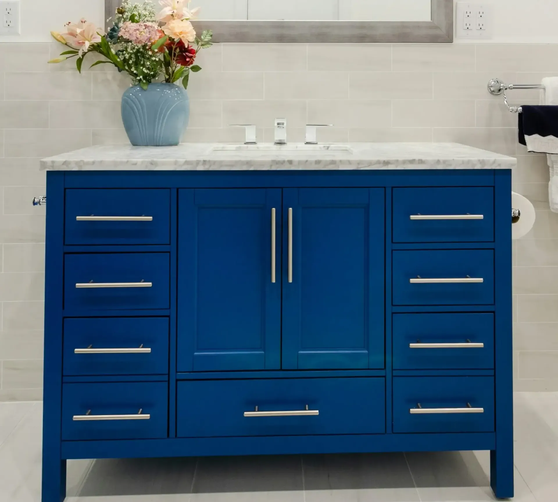 A blue vanity in a bathroom with a vase of flowers on top of it