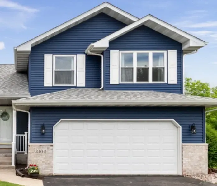A blue house with white shutters and a white garage door