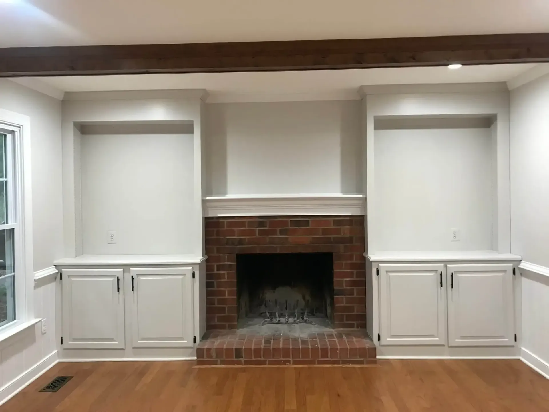 A living room with a brick fireplace and white cabinets.