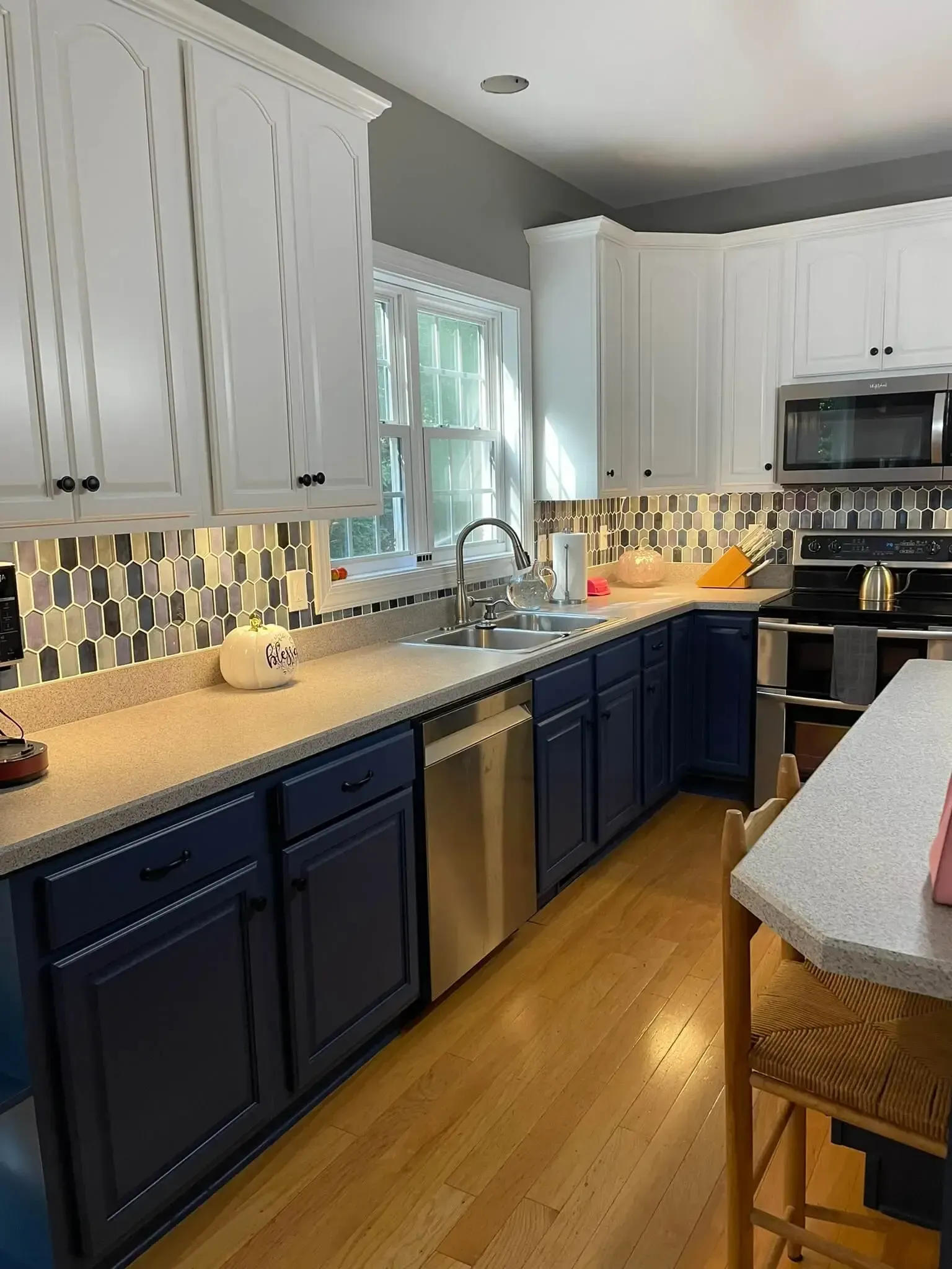 A kitchen with blue cabinets , white cabinets , stainless steel appliances , a sink and a microwave.