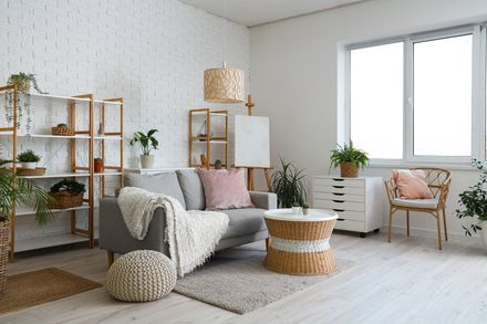 Bright living room with gray sofa, plants, wicker shelves, round table, and large window