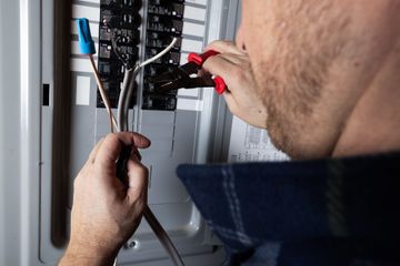 Technician testing electrical panel wires with a multimeter in a utility cabinet