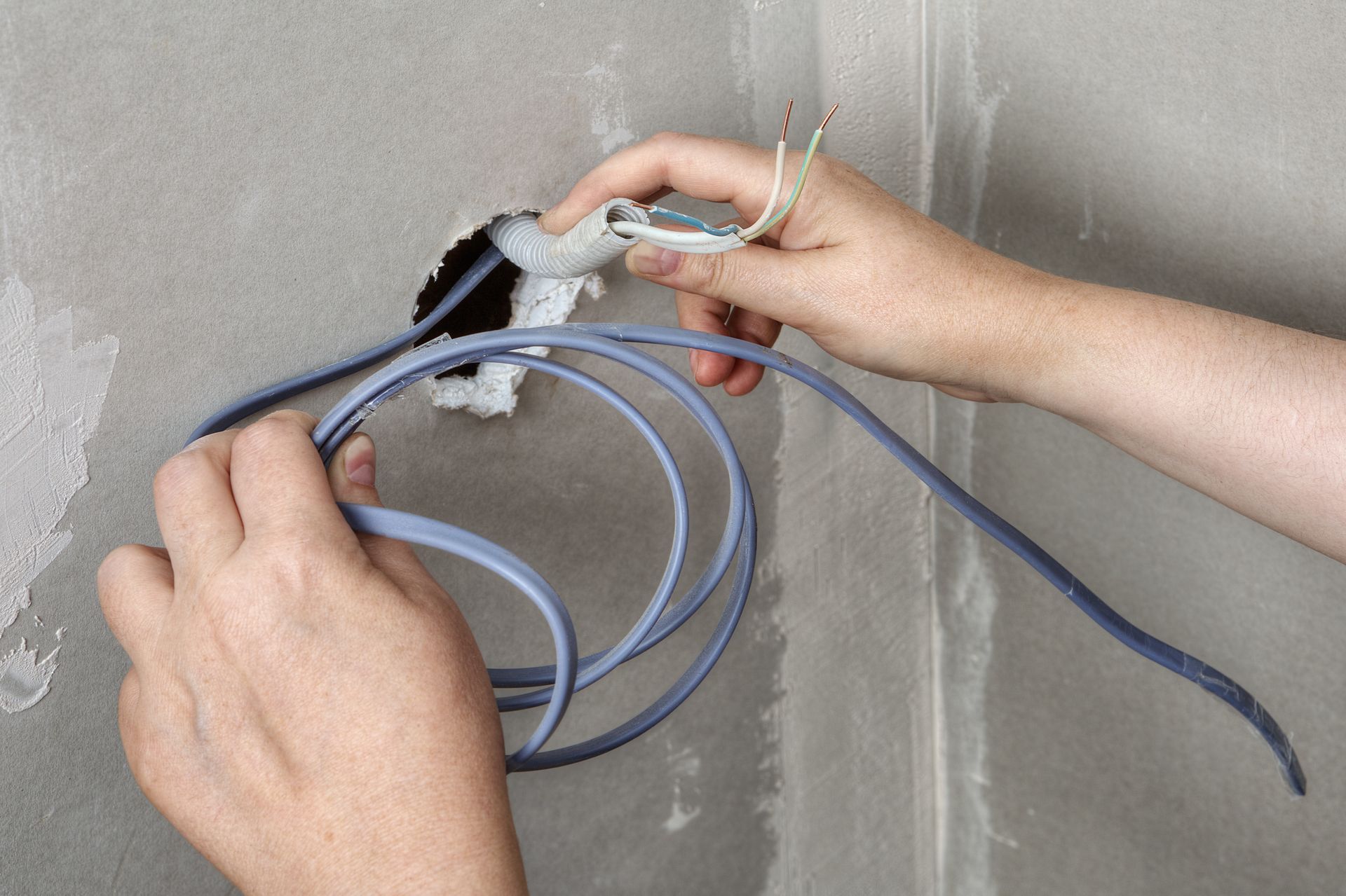 Hands wiring blue cables into a wall outlet box during electrical installation.