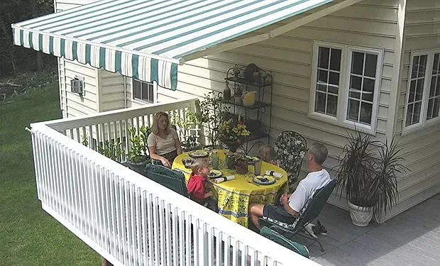 A group of people are sitting at a table on a balcony under an awning.