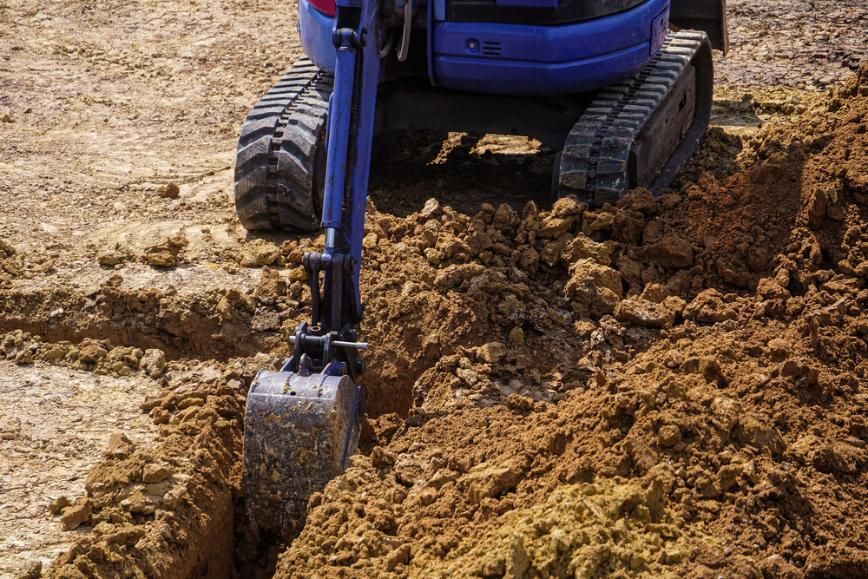 Blue excavator digging in dry dirt at a construction site