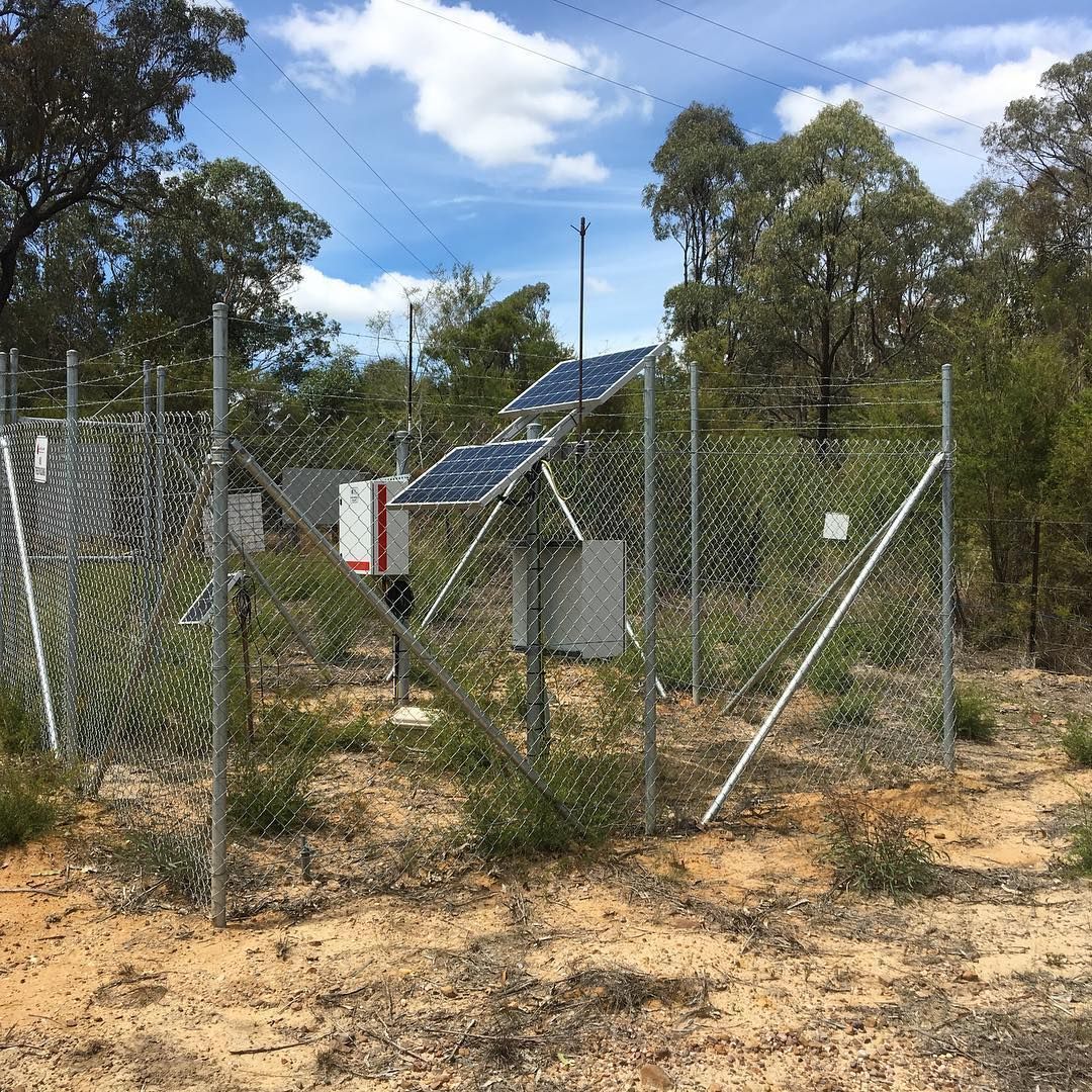 Wire fence with wooden top rail along a wooded dirt path in a rural area