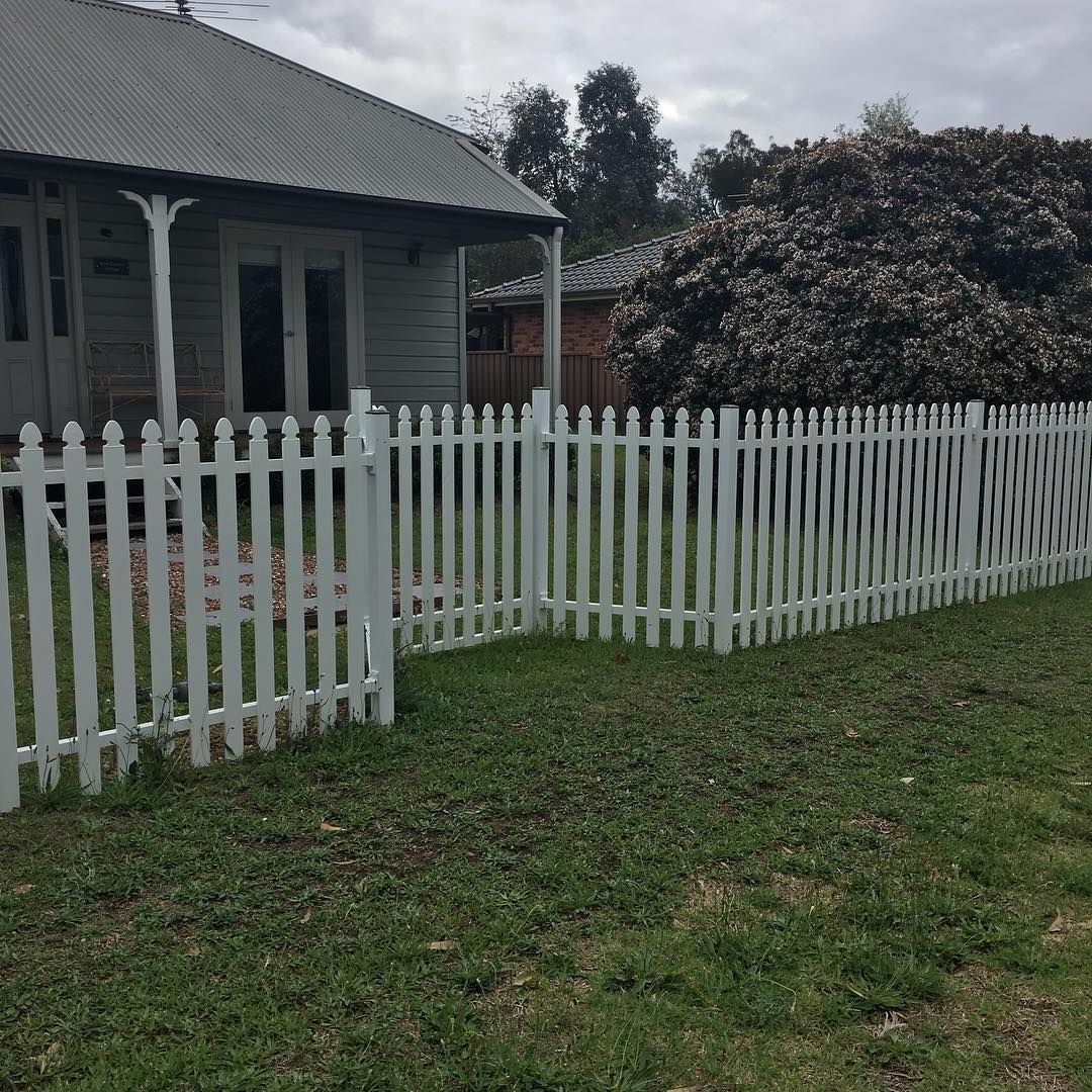 Black wrought-iron fence with stone pillars bordering a green yard and driveway