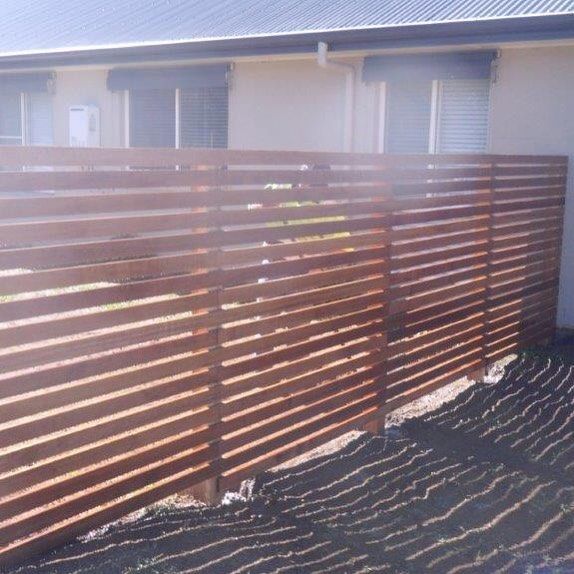 Wooden fence with vertical light-brown slats beside a green yard and sidewalk
