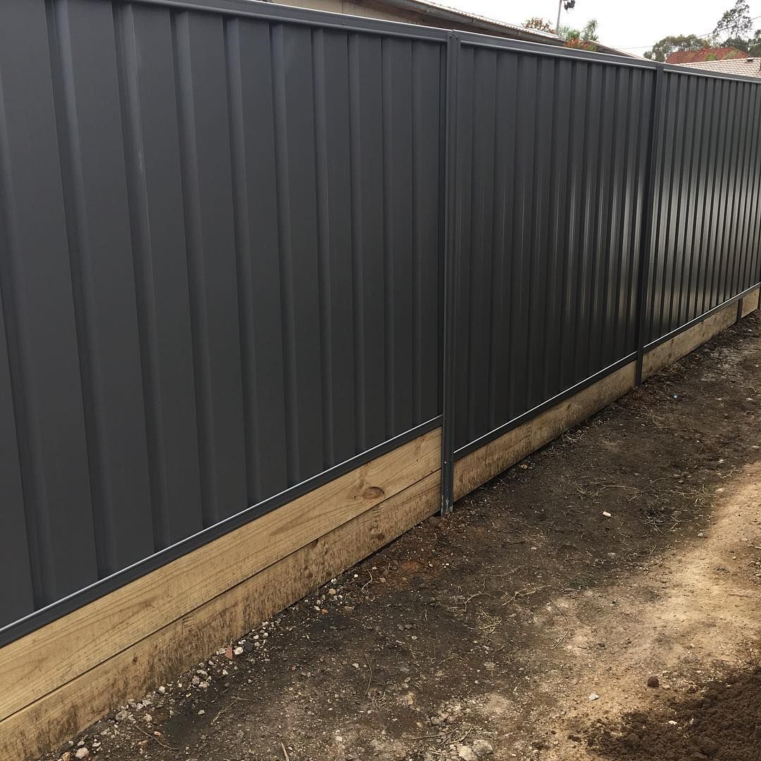 Narrow backyard beside a beige metal fence with grass and dirt under a covered patio.