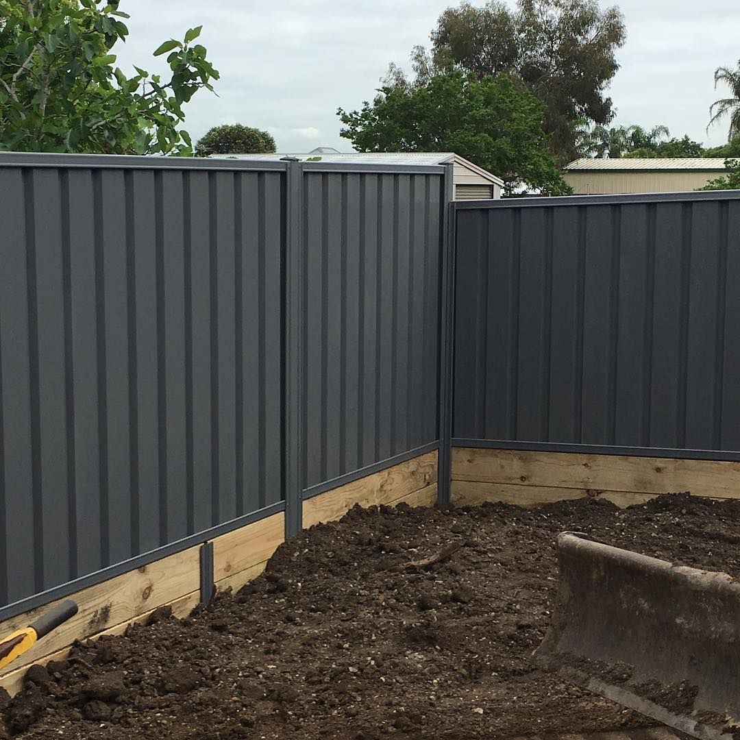 Red metal slat fence with brick pillars along a grassy yard beside a house