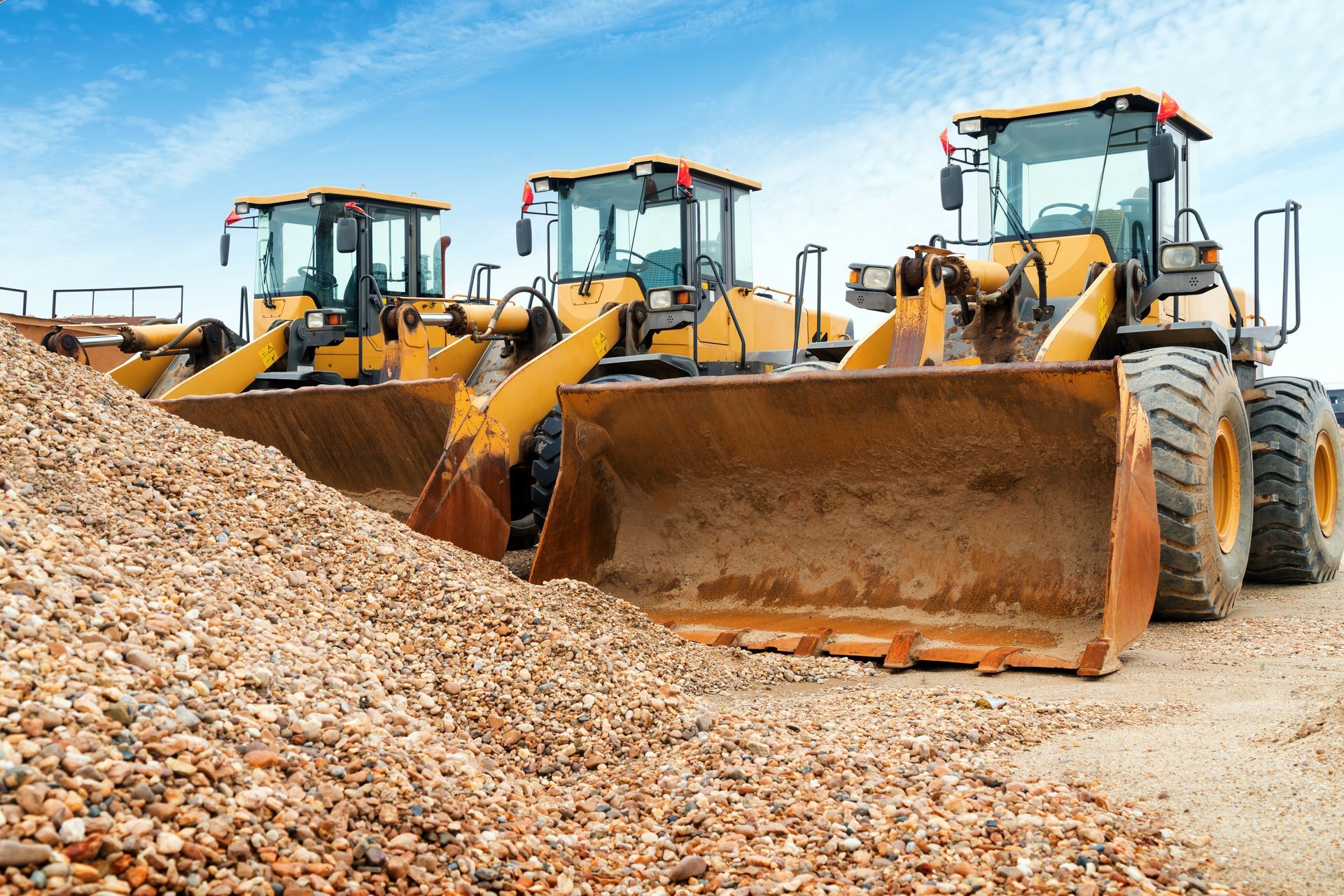 Three yellow front loaders clearing a large gravel pile at a construction site