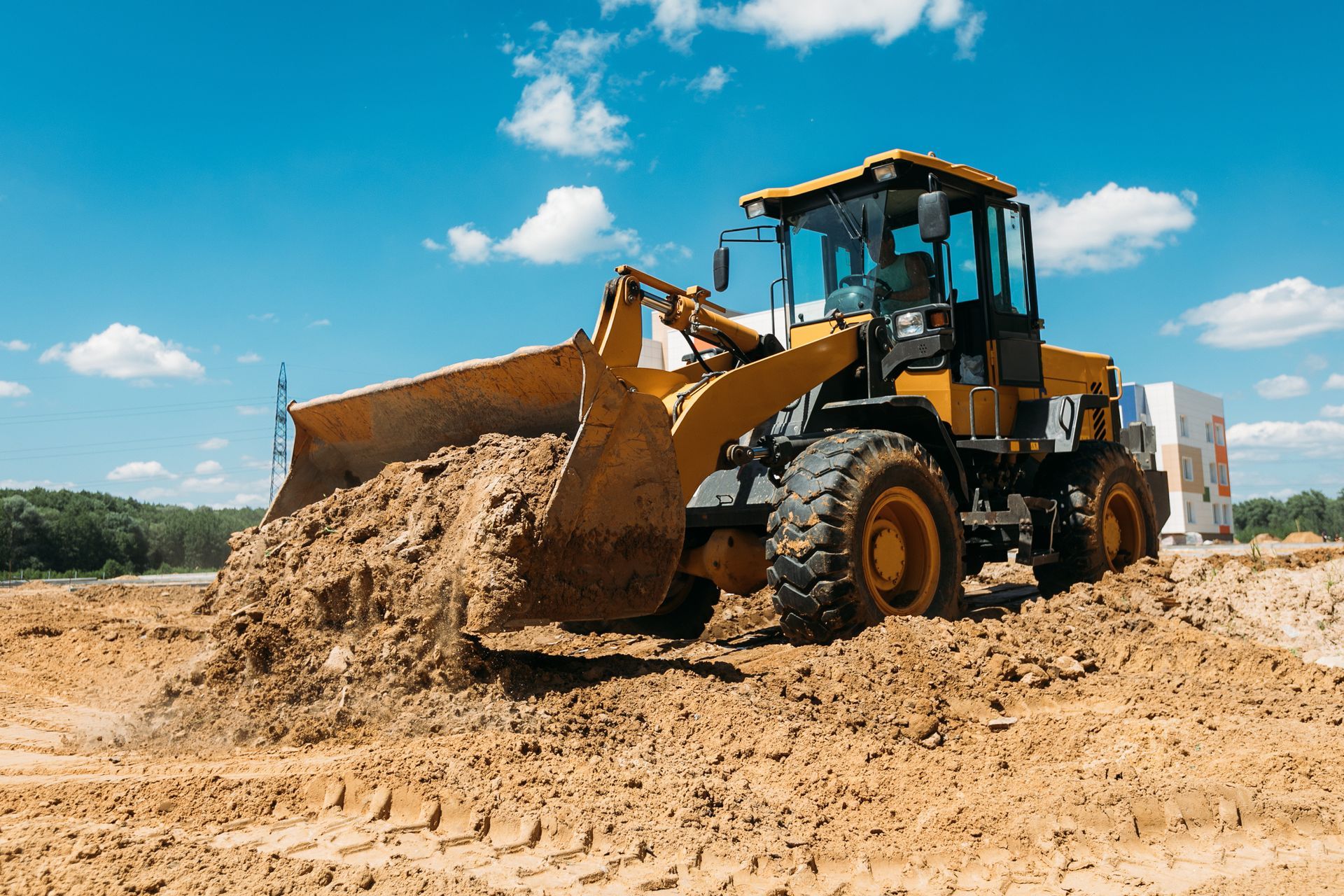 Yellow front loader pushing dirt on a sandy construction site under a blue sky