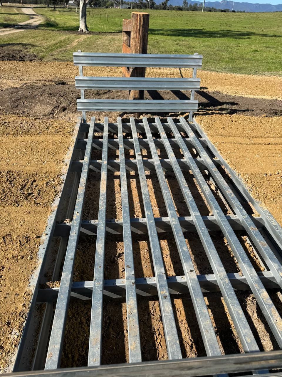 Metal bench and walkway ramp in a sunny park with grass and a wooden post