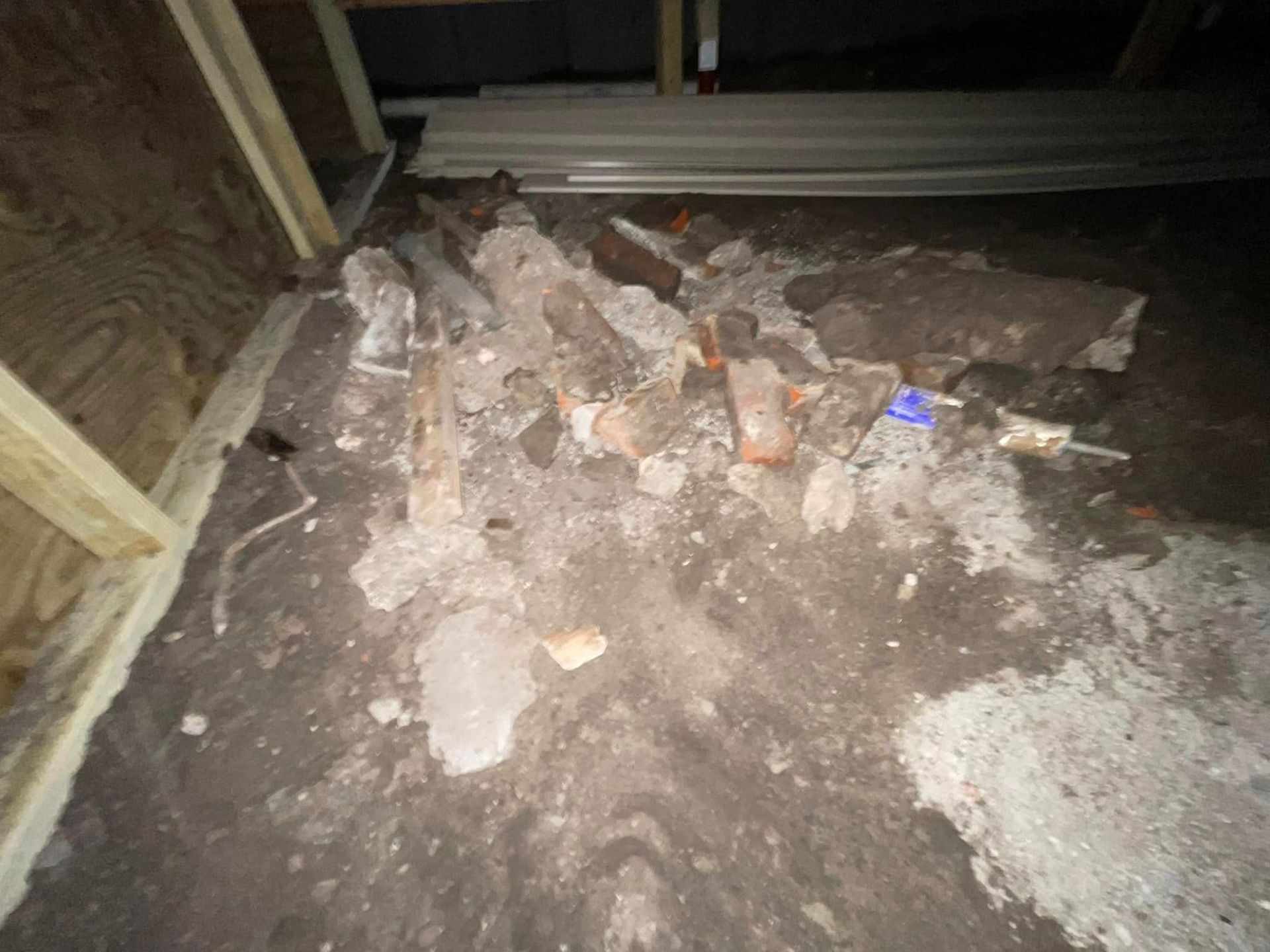 Rubble and broken concrete in a dark construction area with wooden framing and a blue object on the debris.