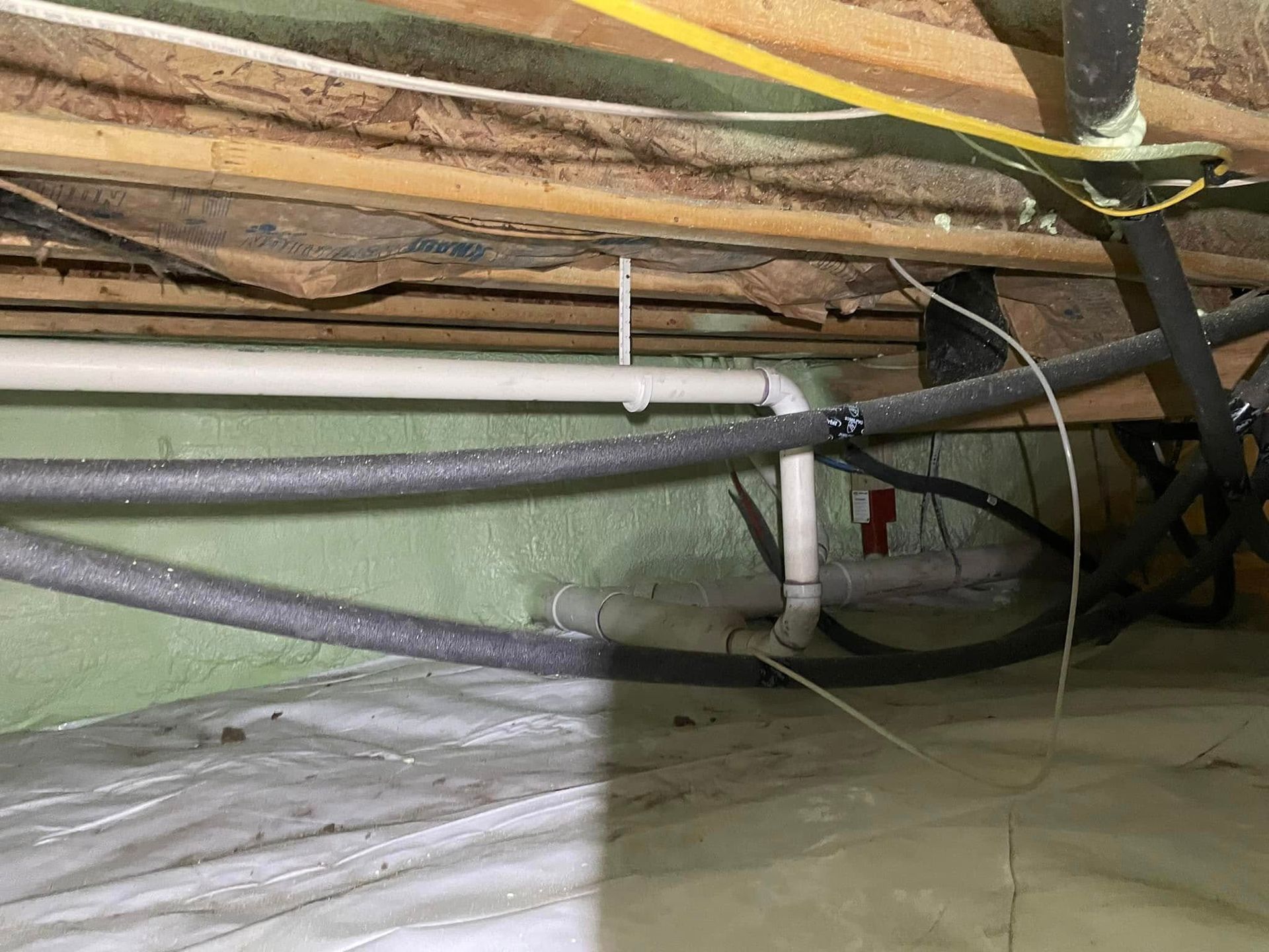 Exposed attic insulation and pipes with black cables and ducting under a slanted wooden roof