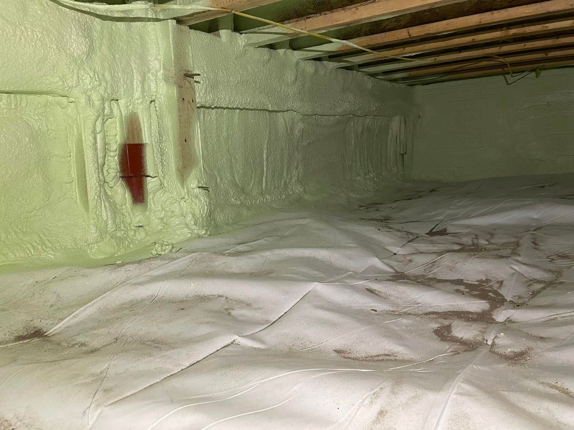 Insulated attic crawlspace with green foam walls, exposed rafters, and white plastic sheeting on the floor