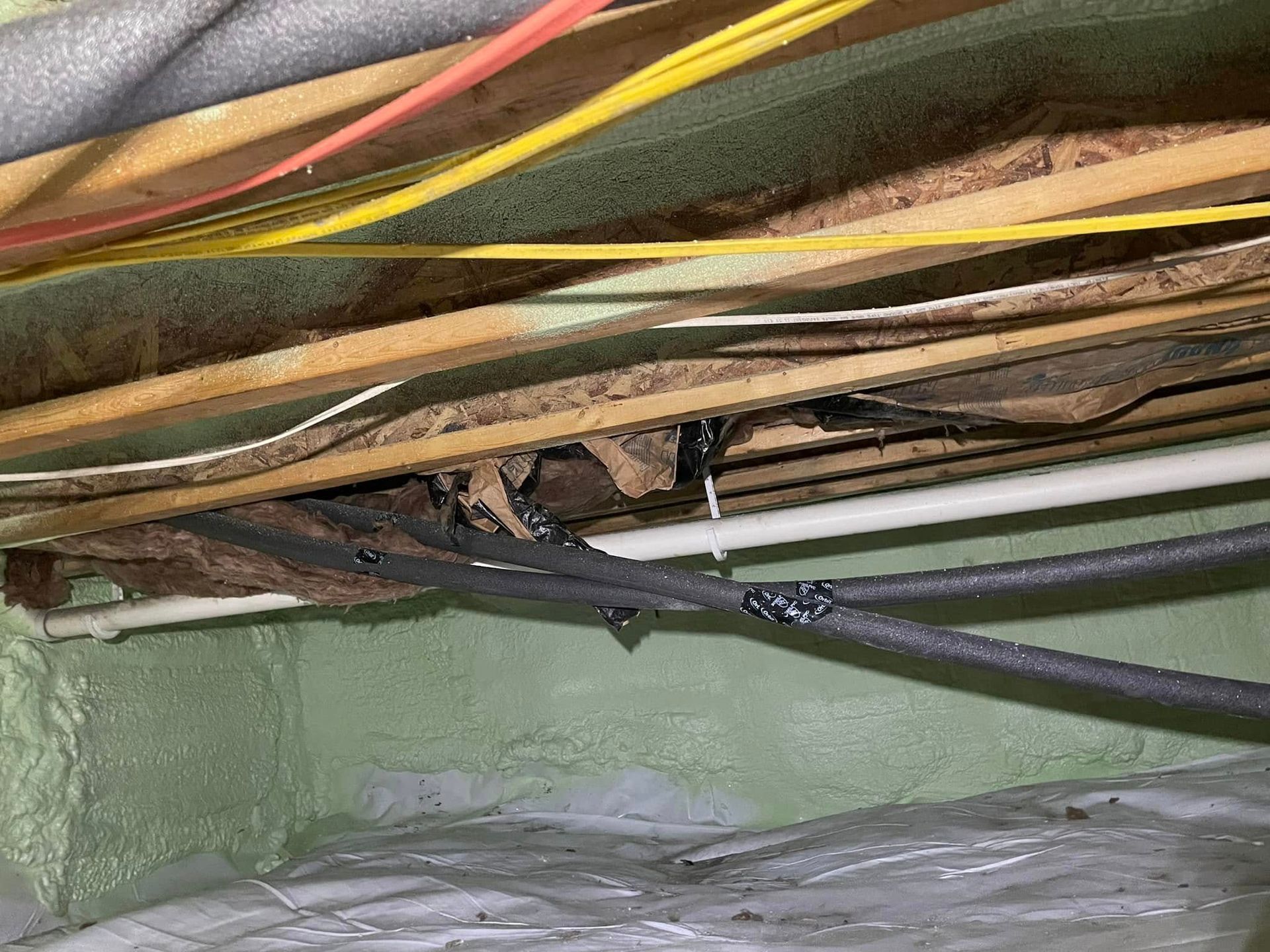 Exposed multicolored wires and cables running through a damaged attic ceiling above green wall framing
