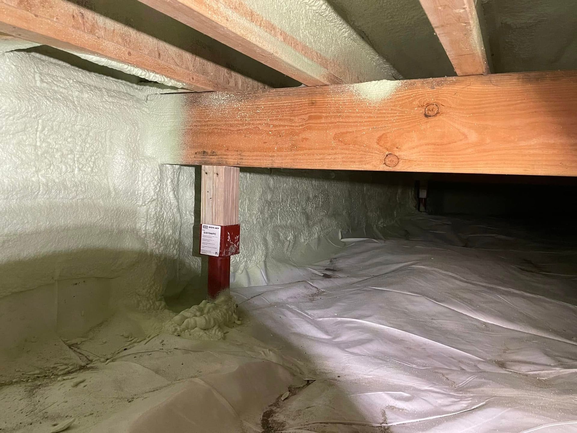 Crawlspace with exposed wooden beams, insulated walls, and a red pipe valve near the floor